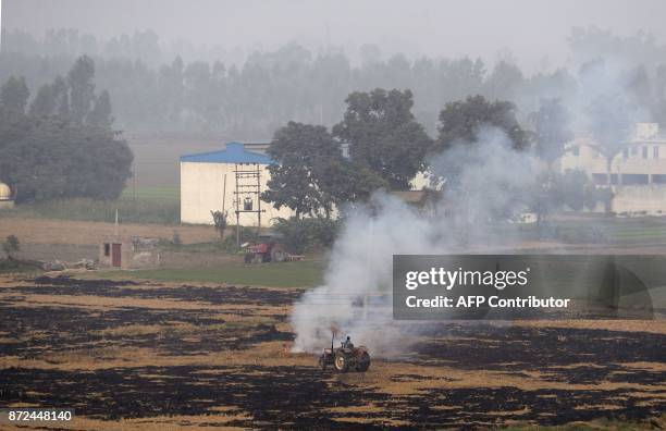 An Indian farmer on a tractor drives past burning paddy stubble in a field on the outskirts of Jalandhar in the northern state of Punjab on November...