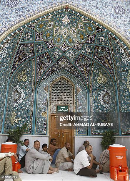 Shiite Muslim men sit in the shade of a tiled arch in the inner courtyard at the Imam Musa al-Kadhim mosque during Friday noon prayers in the...