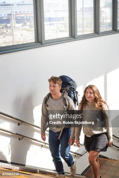 young couple with rucksacks walking up stairs in trainstation - trainstation stock-fotos und bilder