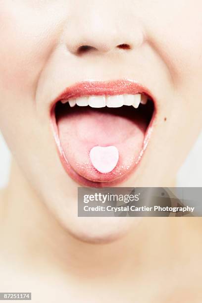 woman with heart-shaped candy on tongue - candy on tongue stock pictures, royalty-free photos & images