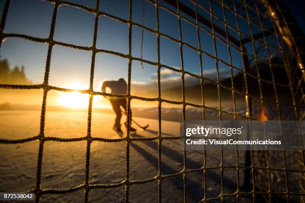 junger mann spielt hockey auf zugefrorenen see. - pond hockey stock-fotos und bilder