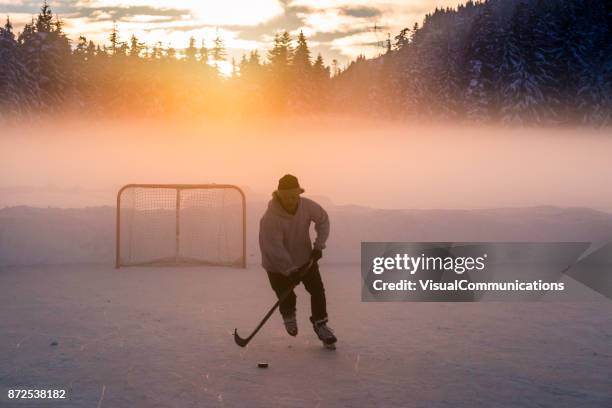 junger mann spielt hockey auf zugefrorenen see. - pond hockey stock-fotos und bilder