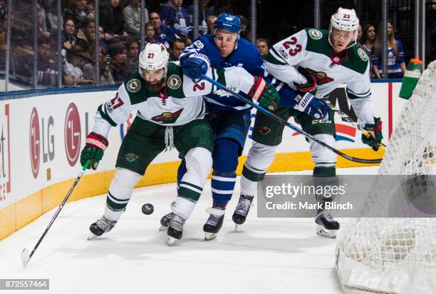 Leo Komarov of the Toronto Maple Leafs battles for the puck with Kyle Quincey and Gustav Olofsson of the Minnesota Wild during the first period at...