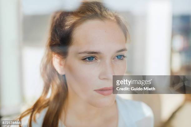 woman looking serious behind a window. - reflection stock-fotos und bilder