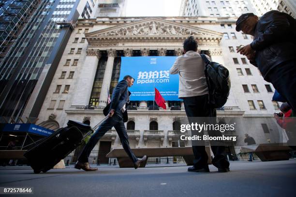 Man pulls luggage while walking past PPDAI Group Inc. Signage displayed in front of the New York Stock Exchange in New York, U.S., on Friday, Nov....