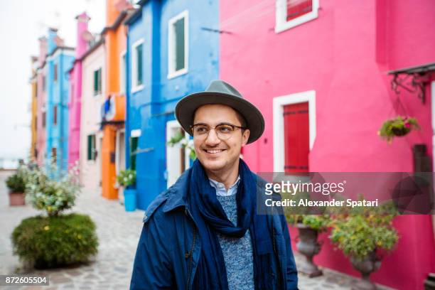young smiling happy man in glasses and hat among colorful houses of burano, italy - burano fotografías e imágenes de stock