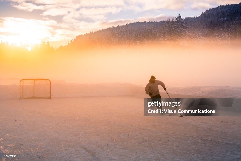 Young man playing hockey on frozen lake.