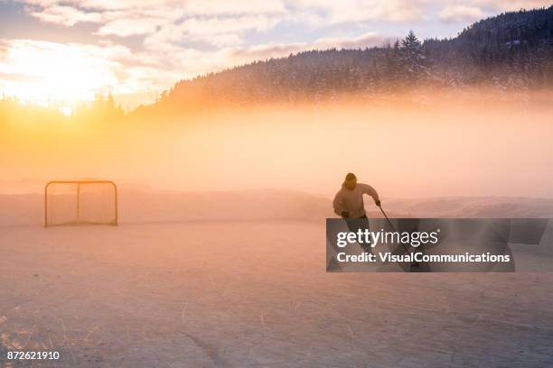 young man playing hockey on frozen lake. - pond hockey stock pictures, royalty-free photos & images