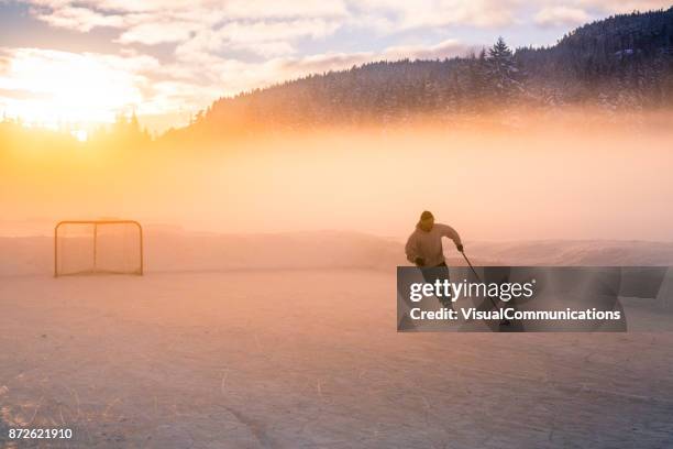 young man playing hockey on frozen lake. - cold man ice stock pictures, royalty-free photos & images