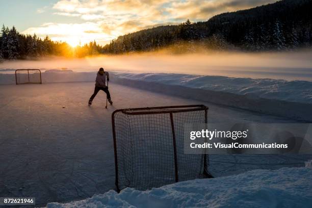junger mann spielt hockey auf zugefrorenen see. - pond hockey stock-fotos und bilder