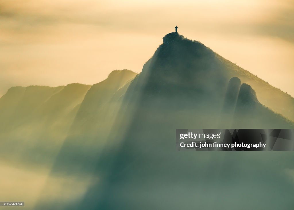 A Lone man stands on a jagged hill in misty conditions at sunrise, English Peak District. UK.