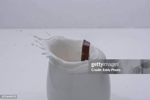 barra de chocolate salpicando al caer en vaso de leche - caer stockfoto's en -beelden