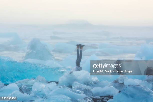 a person doing a handstand at the diamond ice beach at jokulsarlon, iceland - den kopf in den sand stecken stock-fotos und bilder