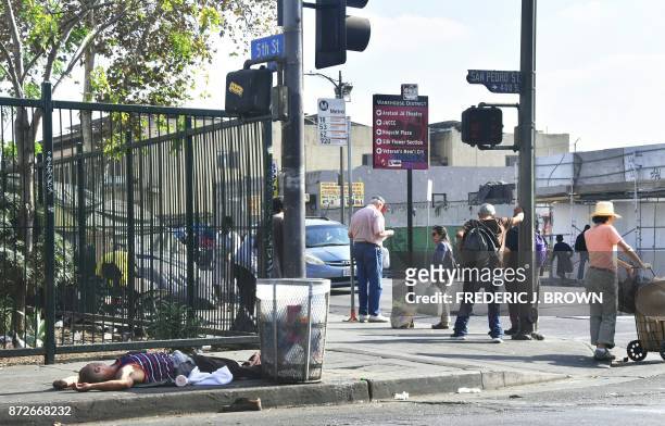 People wait at a bus stop as a man lays passed out on the street, November 10, 2017 in Los Angeles, California, home to one of the nation's largest...