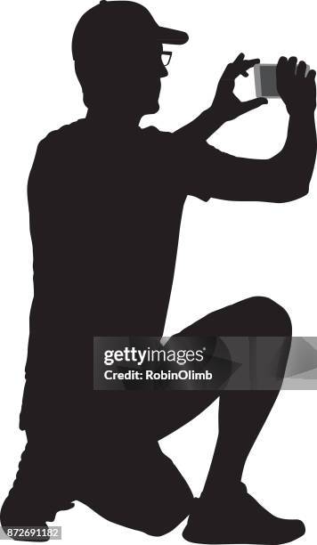 stockillustraties, clipart, cartoons en iconen met knielende man nemen van foto met slimme telefoon - hurken