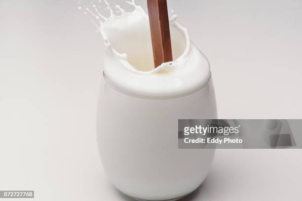 barra de chocolate salpicando al caer en vaso de leche - vaso stock-fotos und bilder