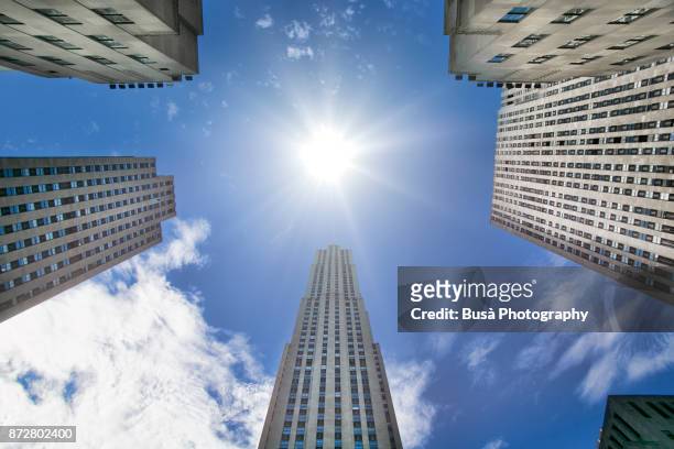 view from below of 30 rockefeller plaza, surrounded by other buildings comprising the rockefeller center, in midtown manhattan, new york city - 30 rockefeller plaza stock pictures, royalty-free photos & images