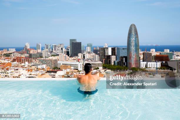 young guy sunbathing in swimming pool and looking at barcelona skyline - rooftop pool stock pictures, royalty-free photos & images