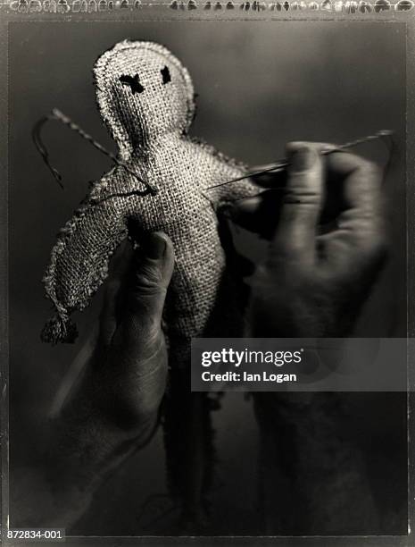 hand pushing pin into voodoo doll (b&w) - voodoo doll stock pictures, royalty-free photos & images