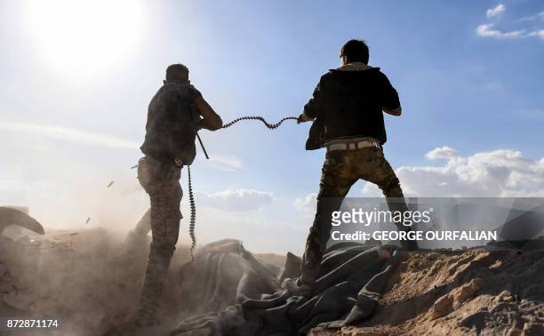 Member of the Syrian pro-regime forces fires a machine gun as a comrade holds his feeding ammunition belt, during the advance towards rebel-held...