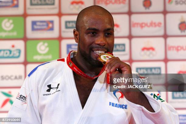 France's gold medallist Teddy Riner bites his gold medal as he celebrates on the podium after defeating Belgium's Toma Nikiforov during the Judo...