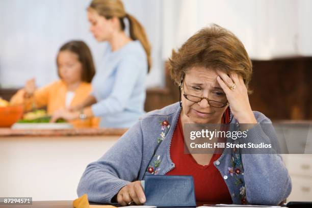 worried hispanic woman writing checks in kitchen - social projects address needs of struggling families stockfoto's en -beelden