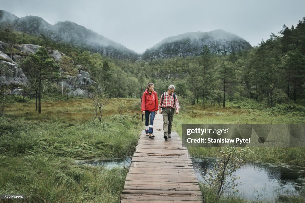 Two hikers passing through a brook on wooden bridge