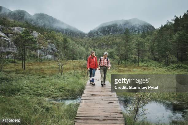 two hikers passing through a brook on wooden bridge - red jacket stock pictures, royalty-free photos & images