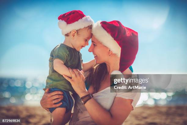 kleine jongen en zijn moeder op kerstmis op het strand - christmas summer stockfoto's en -beelden