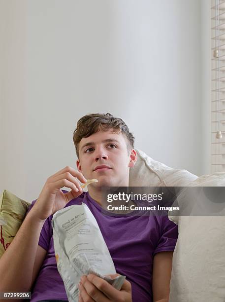 young man eating a packet of crisps - potato chips stock pictures, royalty-free photos & images