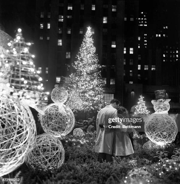 Pair of lovers are entranced by the beauty of the scene after the traditional Rockefeller Center Christmas tree was lighted. The couple is framed by...