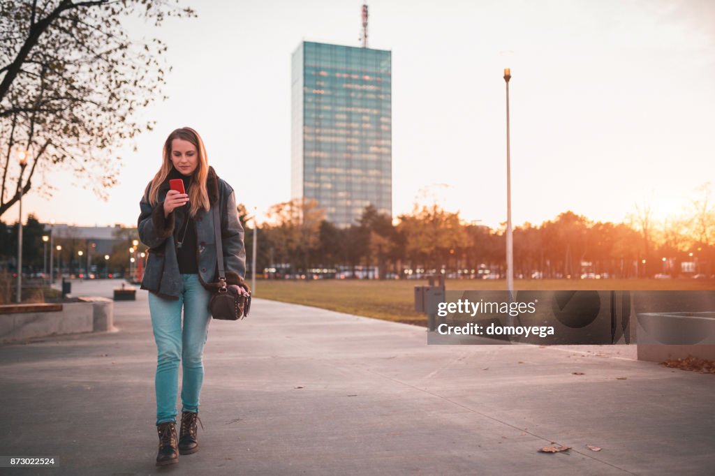 Young woman walking through the park and using phone