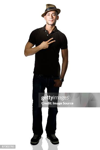 portrait of a young man holding two fingers up - sombrero fedora fotografías e imágenes de stock