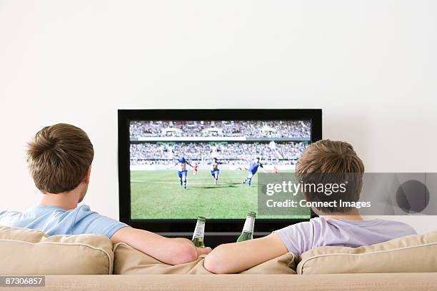 two young men watching football on the tv - man cave stock pictures, royalty-free photos & images