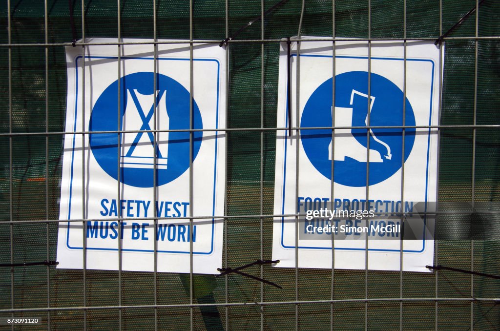 SAFETY VEST MUST BE WORN and FOOT PROTECTION MUST BE WORN signs on the fence around a construction site
