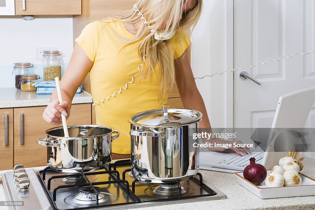 Woman cooking whilst on telephone and using laptop