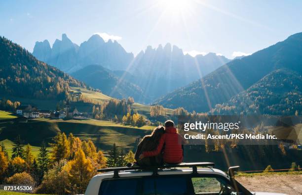 couple sit on car rooftop looking at mountains in the distance - mujer de espaldas en paisaje fotografías e imágenes de stock
