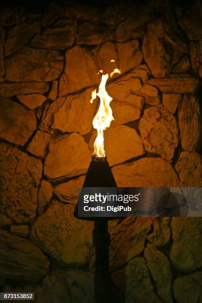 hawaiian cone tiki torch against stone wall in the night - たいまつ ストックフォトと画像