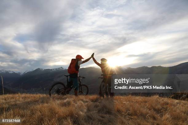 mountain bikers exchange high five on mountainous ridge - euforie stockfoto's en -beelden