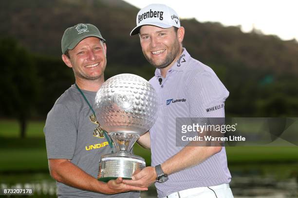 Branden Grace of South Africa poses with the trophy and his brother after his victory during the final round of the Nedbank Golf Challenge at Gary...