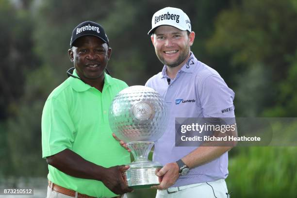 Branden Grace of South Africa poses with caddie Zak Rasego and the trophy after his victory during the final round of the Nedbank Golf Challenge at...