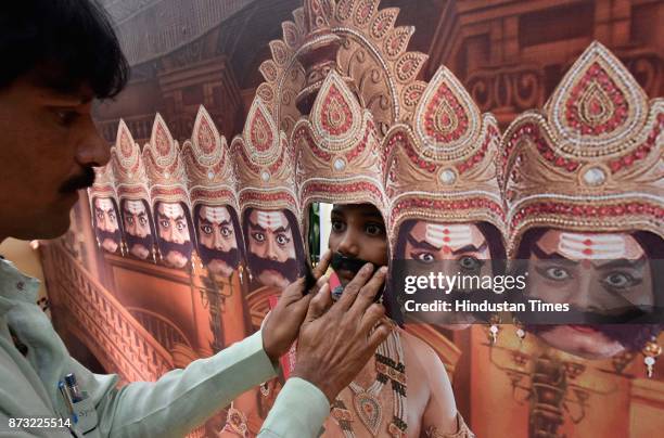 Child wearing a moustache while posing with the cut-out of Ravana during Makkala Hanna, Children Festival at Cubbon Park, on November 12, 2017 in...