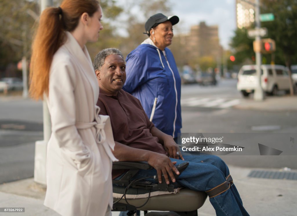 The White teenager girl talking with disabled wheel-chaired African American man and woman when they walking on the street together