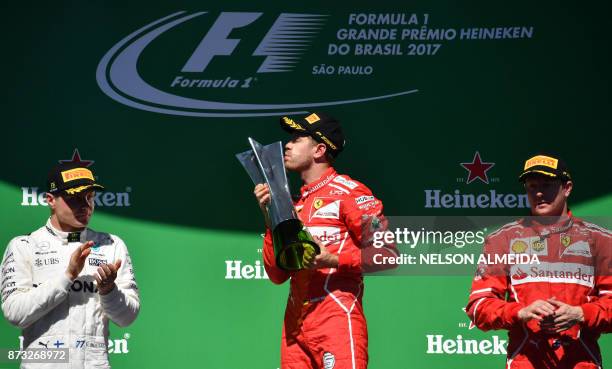 Ferrari's German driver Sebastian Vettel kisses his trophy on the podium next to runner-up Mercedes' Finnish driver Valtteri Bottas and third-place...