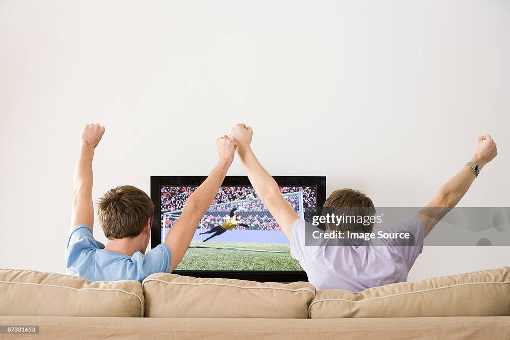 Two young men cheering at football on the tv