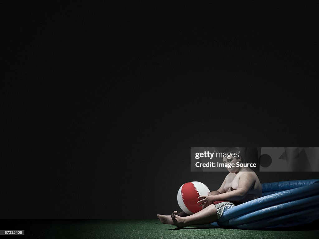 Boy in paddling pool with beach ball