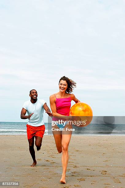 young couple playing with beach ball on the beach - swimwear singlet stock pictures, royalty-free photos & images