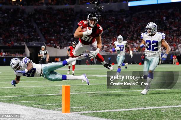 Austin Hooper of the Atlanta Falcons leaps over Xavier Woods of the Dallas Cowboys in an attempt to score a touchdown during the second half at...