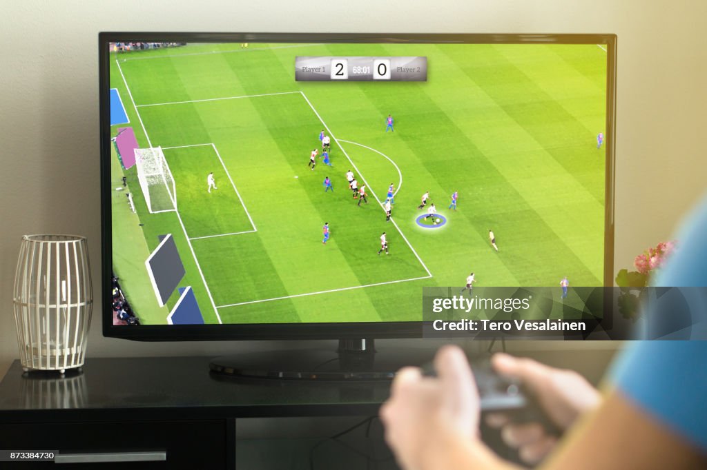 Young man hanging out and playing imaginary soccer or football video game with console and tv.
