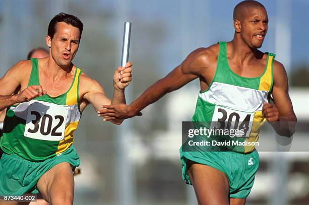 relay race, competitor passing baton to team-mate - track and field baton stock pictures, royalty-free photos & images